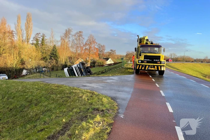 Vrachtwagen belandt op zijn kant onderaan dijk