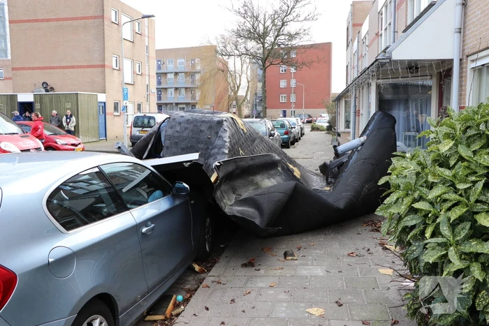 Dakbedekking van flat waait over auto's en lantaarnpalen