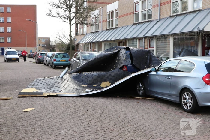 Dakbedekking van flat waait over auto's en lantaarnpalen