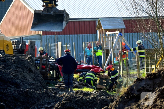 Persoon bekneld onder omgevallen graafmachine