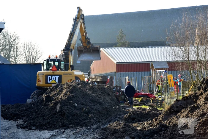 Persoon bekneld onder omgevallen graafmachine