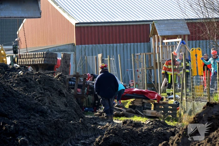 Persoon bekneld onder omgevallen graafmachine