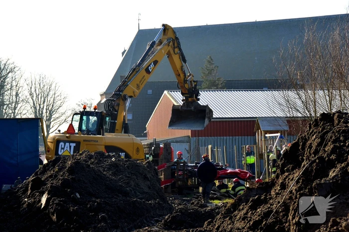 Persoon bekneld onder omgevallen graafmachine