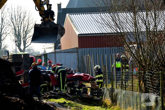 Persoon bekneld onder omgevallen graafmachine