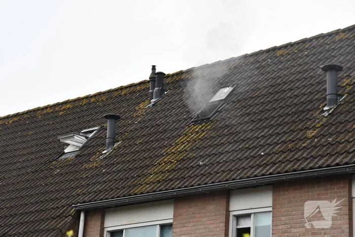 Veel rook uit zolderraam bij brand in woning