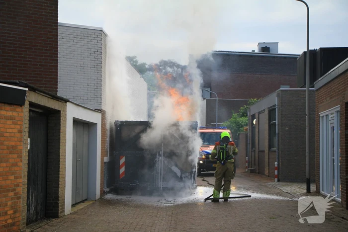 Vlammen slaan uit bouwcontainer met afval