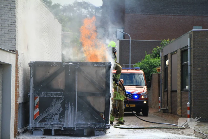 Vlammen slaan uit bouwcontainer met afval