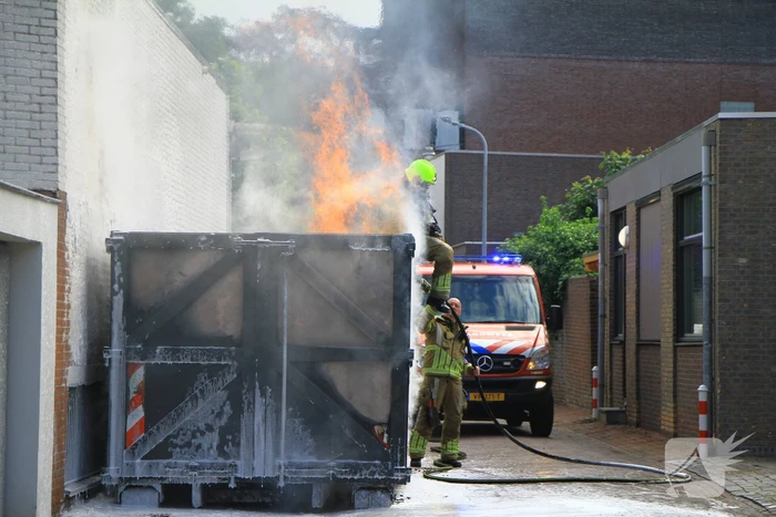 Vlammen slaan uit bouwcontainer met afval