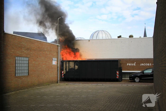 Vlammen slaan uit bouwcontainer met afval