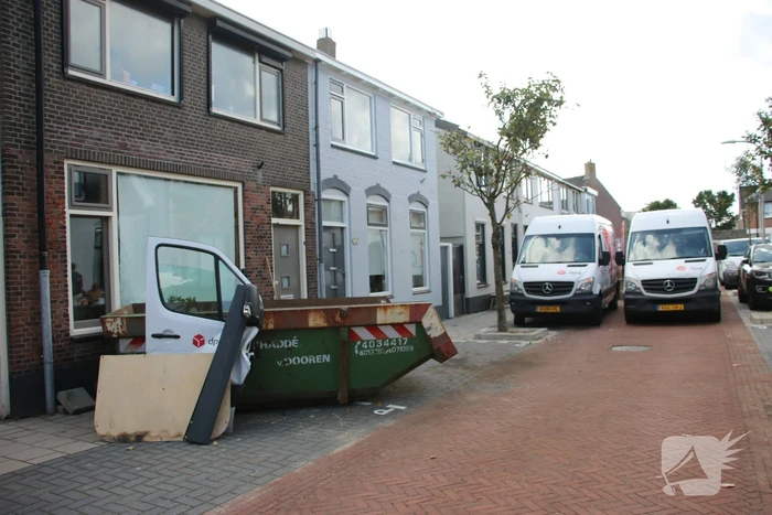 Pakketbezorger botst tegen bouwcontainer en knalt tegen woning