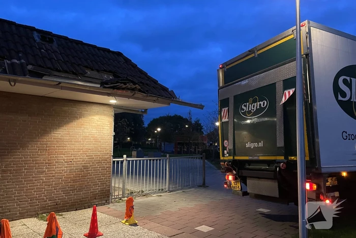 Vrachtwagen rijdt tegen dak van gebouw