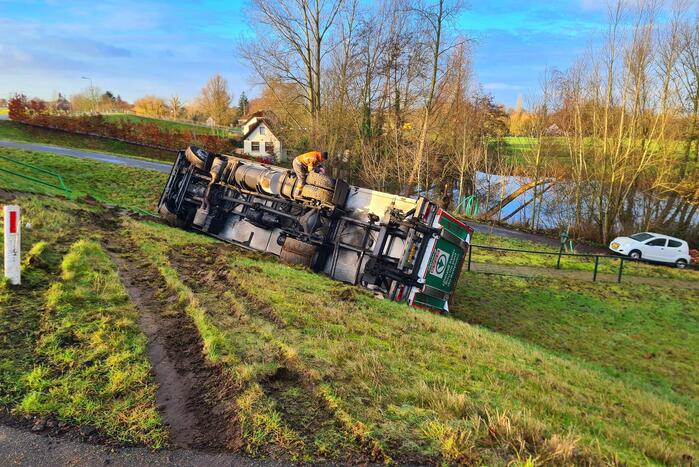 Vrachtwagen belandt op zijn kant onderaan dijk