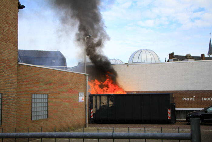 Vlammen slaan uit bouwcontainer met afval