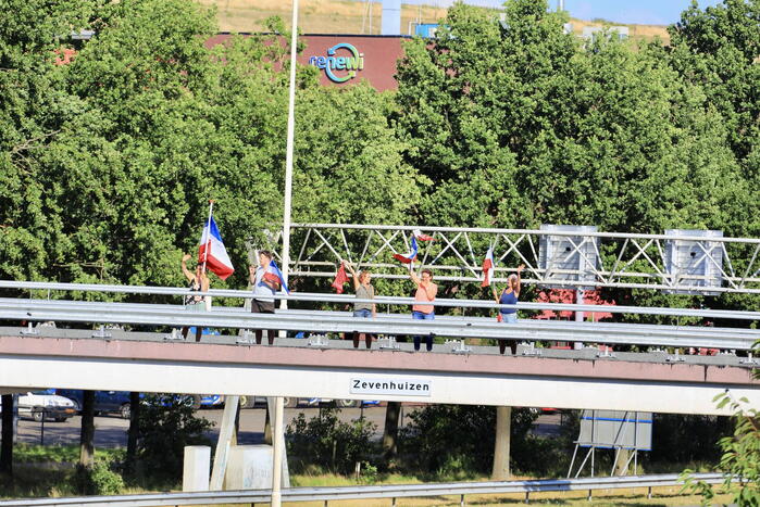 Verontrustende burgers staan met omgekeerde vlaggen zwaaien naar verkeer op A1