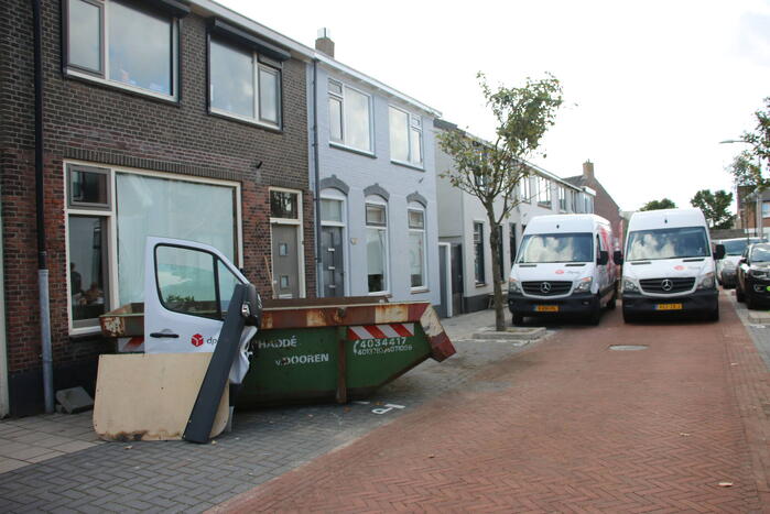 Pakketbezorger botst tegen bouwcontainer en knalt tegen woning