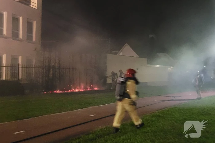Brandweer blust brandend heg naast pand