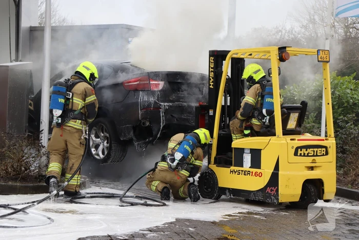 Auto vliegt in brand voor ingang carwash