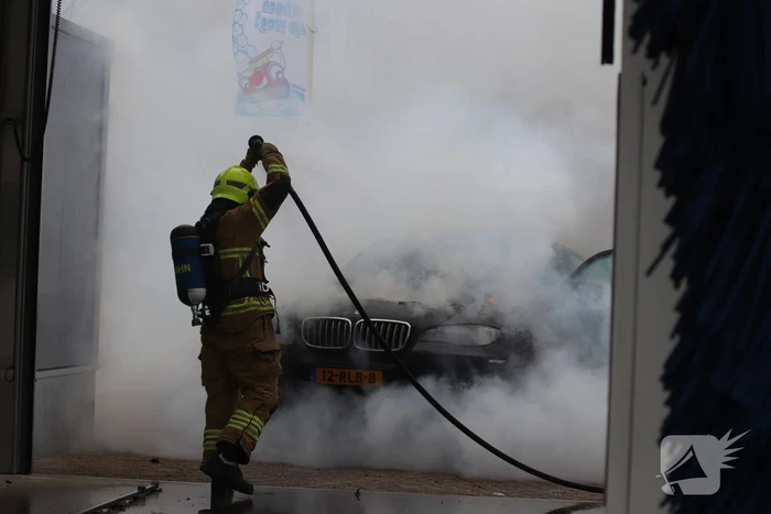 Auto vliegt in brand voor ingang carwash