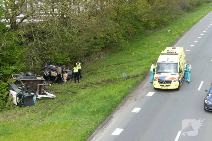Auto en aanhanger met graafmachine over de kop