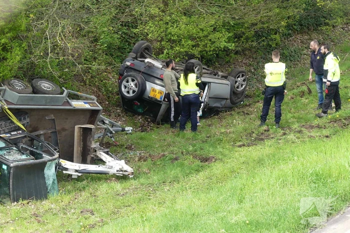 Auto en aanhanger met graafmachine over de kop
