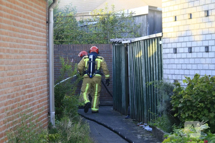 Brandweer blust brandende prullenbak in schuur
