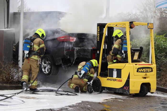 Auto vliegt in brand voor ingang carwash