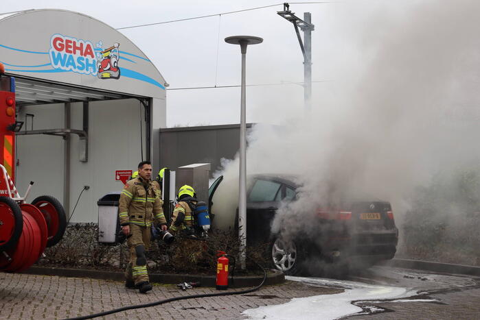 Auto vliegt in brand voor ingang carwash
