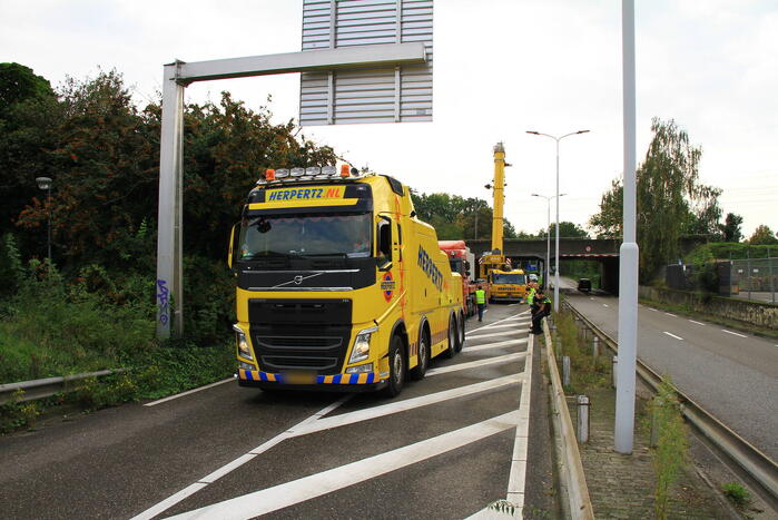 Vrachtwagen geladen met betonplaten vast onder spoorbrug
