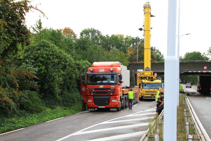 Vrachtwagen geladen met betonplaten vast onder spoorbrug