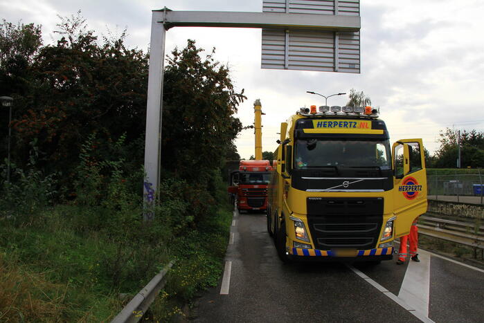 Vrachtwagen geladen met betonplaten vast onder spoorbrug