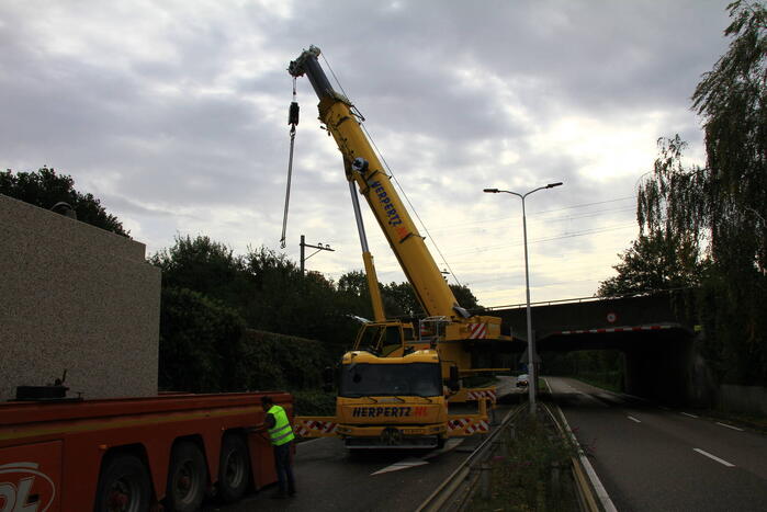 Vrachtwagen geladen met betonplaten vast onder spoorbrug