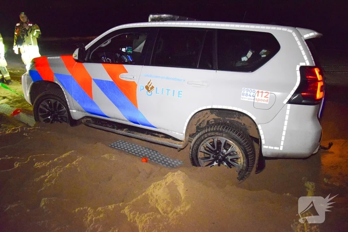 Politiejeep muurvast in los zand op strand