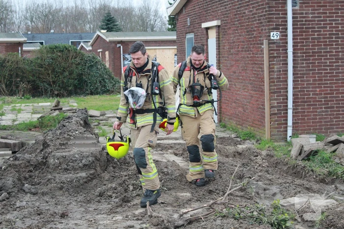 Brandweer blust brandend afval achter sloopwoningen