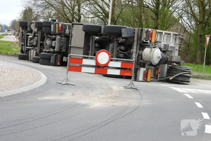Vrachtwagencombinatie met zand kantelt op rotonde