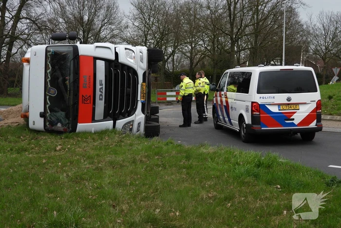 Vrachtwagencombinatie met zand kantelt op rotonde