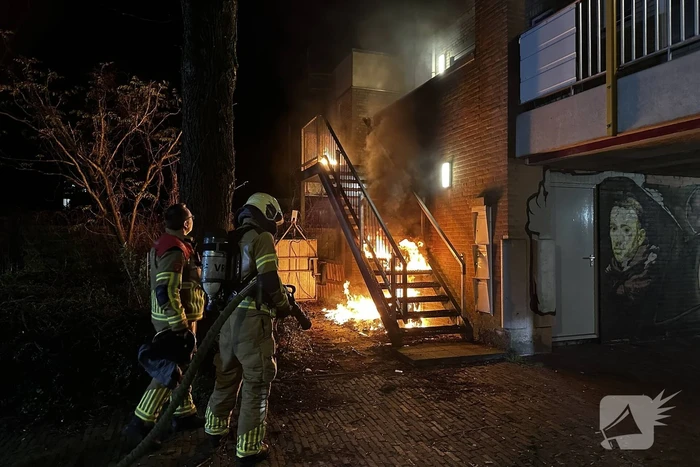 Brandweer blust brandende container onder trap
