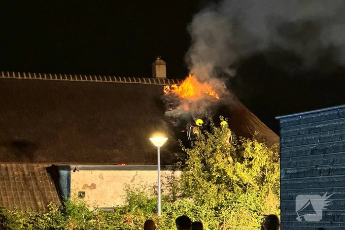 Vlammen slaan uit rietendak van woning