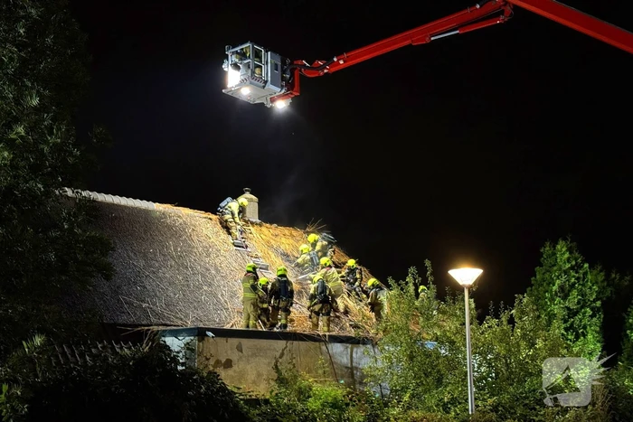 Vlammen slaan uit rietendak van woning