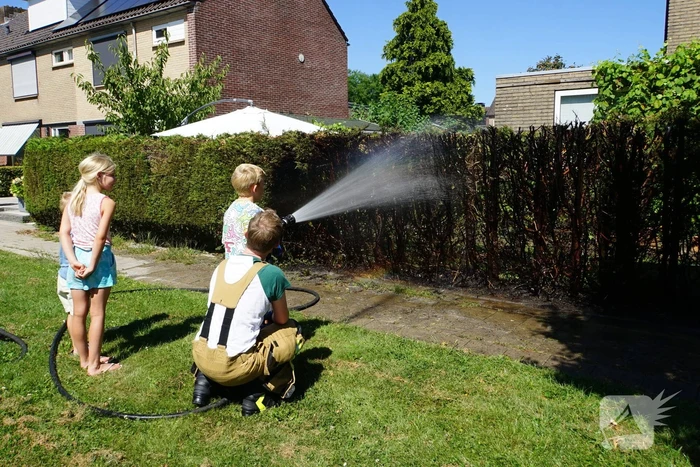 Kinderen blussen met brandweer brandende coniferenhaag