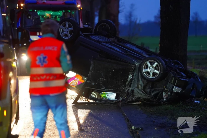 Auto op de kop na botsing met trekker en boom
