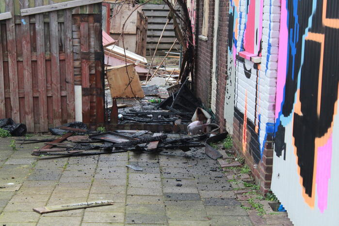 Brandweer blust brandend afval achter sloopwoningen