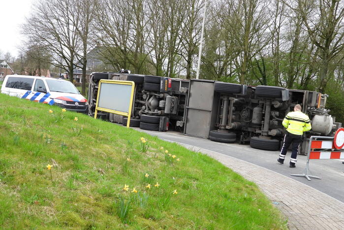 Vrachtwagencombinatie met zand kantelt op rotonde