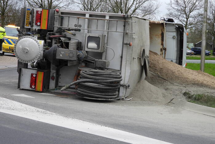 Vrachtwagencombinatie met zand kantelt op rotonde