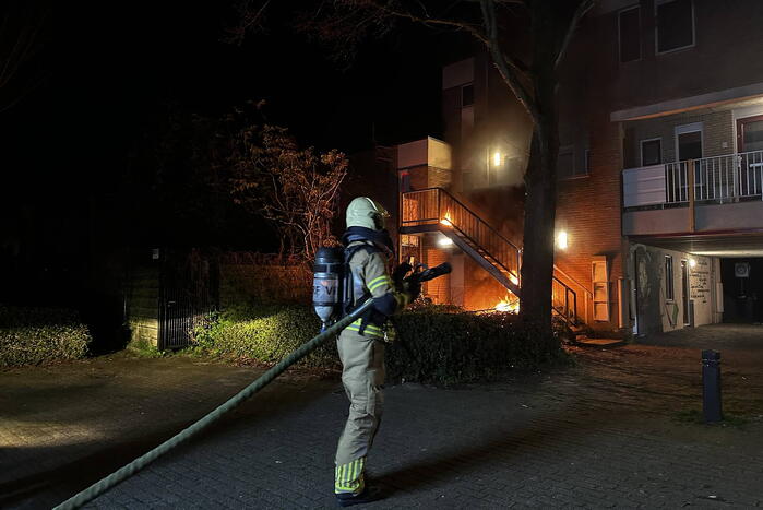 Brandweer blust brandende container onder trap