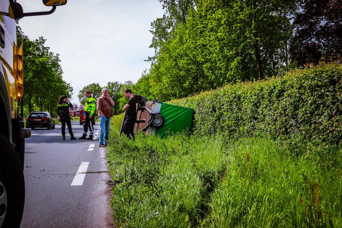 Aanhanger geladen met stenen belandt op zijn kant