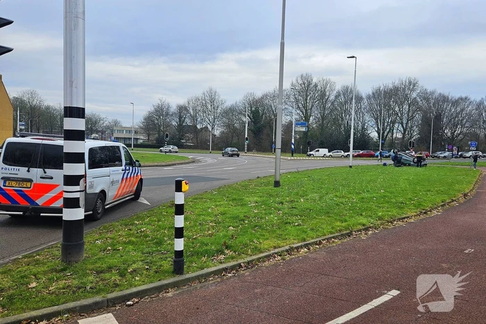Auto belandt op kop naast rotonde