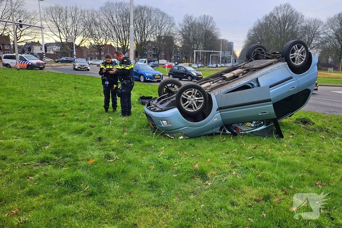 Auto belandt op kop naast rotonde