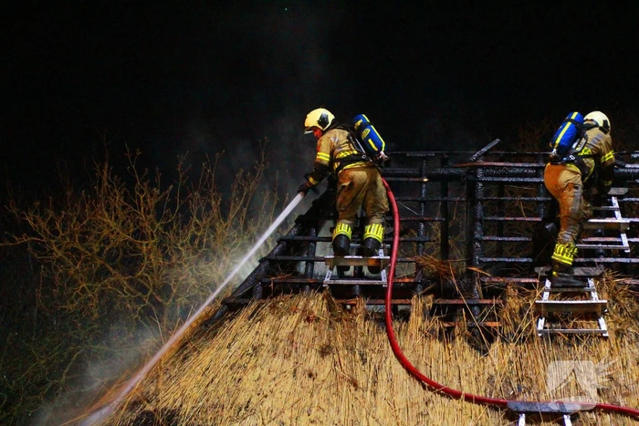 Brandweerlieden trekken rietendak uit elkaar om brand te kunnen bestrijden