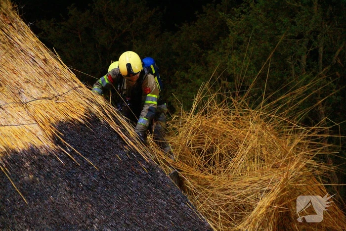 Brandweerlieden trekken rietendak uit elkaar om brand te kunnen bestrijden