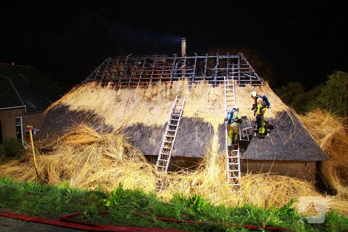 Brandweerlieden trekken rietendak uit elkaar om brand te kunnen bestrijden
